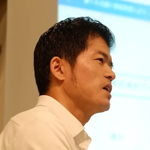 代表の川添祐樹。白いシャツで、スライドを映した画面の前で話している